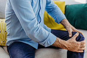 Man sitting on couch, grabbing onto his knee with both hands.