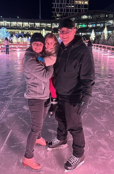 Bre and Mike with their daughter standing on an ice rink and smiling at the camera